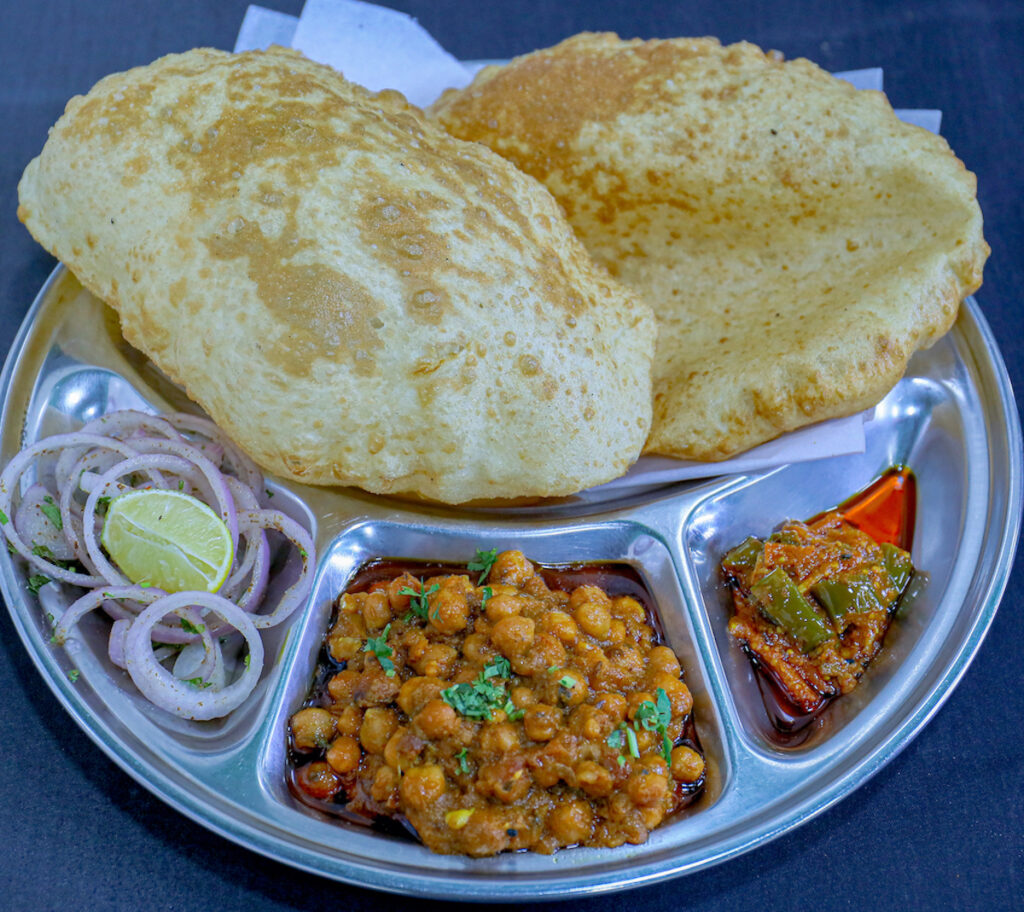 Spicy, slow-cooked chickpea curry (chholey) served with fluffy, golden-fried bhature, raw onion rings, tangy pickle, and green chillies.