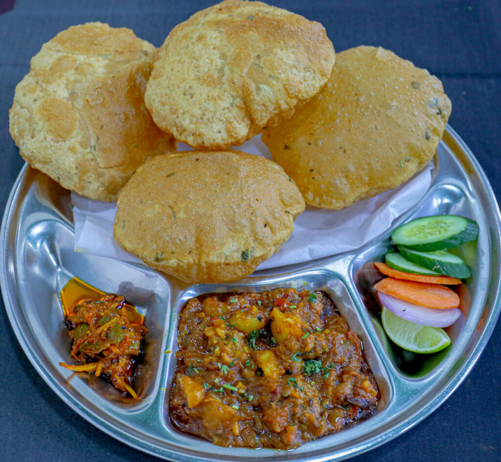 Golden-fried, fluffy whole wheat pooris served hot with a flavorful, mildly spiced potato curry (aloo bhaji), pickled onions, and tangy green chutney.